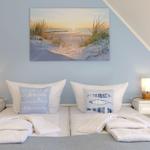 Zwei Betten mit weißen Kissen und Decken unter einem Wandbild mit Strandmotiv.