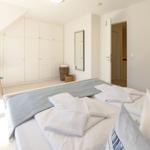 Schlafzimmer mit Dachschrägen, weißer Einbaukombination und Bett mit weißen Bettwäsche und blauen Kissen.