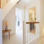 Hausflur mit Holztreppe, kleinem Tisch und Vasen. Blick in Schlafzimmer und Bad.