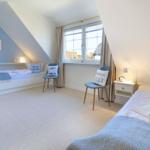 Zimmer mit zwei Betten, Fenster, Stühlen und blauen Kissen.