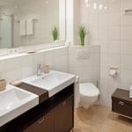 Badezimmer mit zwei Waschbecken, Toilette, Dusche und Holzregal.