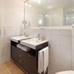Badezimmer mit Doppelwaschbecken, Spiegel und Toilette. Holztreppe im Hintergrund.