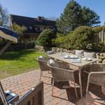 Terrasse mit Tisch und Stühlen, Grünfläche und Holzzaun im Hintergrund.