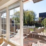 Durchgehende Glasschiebetüren führen auf eine Terrasse mit Tisch und Stühlen.