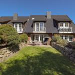 Haus mit Balkon, Terrasse und Garten. Steinmauern umgeben den Rasen.