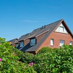 Ein Haus mit rotem Backstein und dunklem Dach, umgeben von grünen Sträuchern und rosa Blüten.