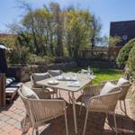 Terrasse mit Tisch, Stühlen und Strandkorb. Grünfläche und Steinmauer im Hintergrund.
