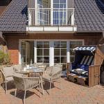Terrasse mit Tisch, Stühlen und Strandkorb vor Haus mit Balkon.