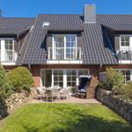 Haus mit Balkon, Terrasse und Gartenbereich. Holz- und Steinmauern umgeben den Außenbereich.