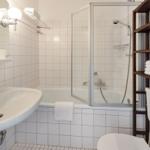 Badezimmer mit Badewanne, Dusche, Waschbecken und Holzregal.