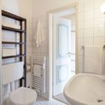 Badezimmer mit Dusche, Waschbecken und Toilette. Weiße Fliesen und Handtücher.