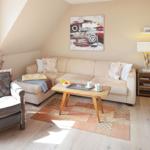 Wohnzimmer mit Sofa, Sessel, Couchtisch und Fernseher. Wandbild und Teppich sind sichtbar.
