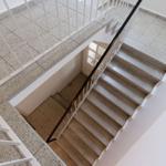 Treppe mit weißem Geländer und dunklem Handlauf. Bodenfliesen und weiße Wände.
