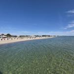 Strand mit klarem Wasser und Strandkörben unter blauem Himmel.