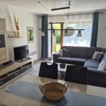 Wohn- und Essbereich mit Sofa, Fernseher und Tisch. Durchgang zur Terrasse.