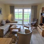 Wohnzimmer mit Sofa, Sessel und Fernseher. Durchgangstür führt auf eine Terrasse mit Blick auf Feld.