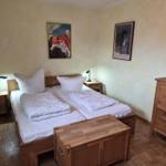 Zimmer mit Doppelbett, zwei Nachttischen und Holzmöbeln. Wandbilder und Spiegel sind vorhanden.