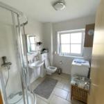 Badezimmer mit Dusche, Waschbecken, Toilette und Fenster.