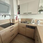 Küche mit Holzfronten, Spüle, Kaffeemaschine und Kühlschrank.
