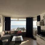 Wohnzimmer mit Sofa, Tisch und Blick aufs Meer durch große Fenster.