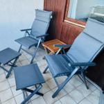 Terrasse mit zwei Liegestühlen und zwei Fußstützen. Holztisch und Holzwand sichtbar.