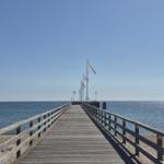 Holzsteg führt über Sandstrand zum Meer mit Flaggen entlang