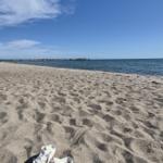 Weißschuhe auf Sandstrand mit Blick auf Meer und Steg.
