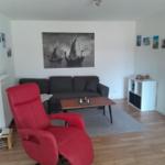 Ein Wohnzimmer mit grauem Sofa, rotem Sessel und Holzboden.