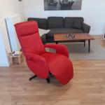Rotes Sessel, graue Couch, Holztisch, Wandbild mit Schiffen.