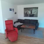 Ein Wohnzimmer mit grauem Sofa, rotem Sessel und Holzboden. An der Wand hängt ein großes Bild von Schiffen.