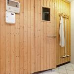 Sauna mit Holzwand, Steuerung und Handtuchhalter. Fliesenboden und Fenster.