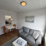 Wohnzimmer mit Sofa, Tisch und Bild an der Wand. Küche im Hintergrund.