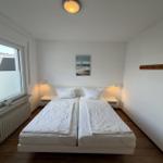 Schlafzimmer mit Doppelbett, Fenster und Wandbild. Holzboden und Deckenleuchte.