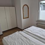 Zwei Betten, Kleiderschrank, Spiegel und Fenster mit Heizkörper.