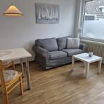 Wohnzimmer mit Sofa, Tisch und Stühlen. Wandbild mit Segelbooten und großes Fenster.
