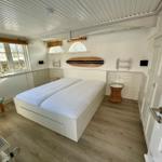 Schlafzimmer mit Doppelbett, Fenstern und Surfbrett an der Wand.