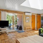 Wohnzimmer mit Kamin, TV und Terrasse. Holzwände und Terrakottaboden.