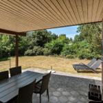 Terrasse mit Tisch, Stühlen und Liegen. Blick auf grünen Garten und Himmel.