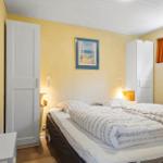 Schlafzimmer mit Bett, Kleiderschrank und Fenster mit orangefarbenen Vorhängen.