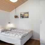 Schlafzimmer mit weißem Bett, Holzdecke und Wandpaneelen. Hängende Pflanze und Bilder an der Wand.