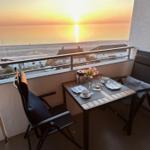 Balcony with table and chairs overlooking sunset over sea and beach.
