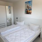 Schlafzimmer mit weißem Bett, Kleiderschrank und Wandbild mit Möwen.
