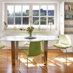 Dining table with green chairs in front of large window with tree view.
