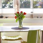Table with flowers, green chairs, and window with garden view.