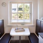 Dining area with table and seating by window overlooking greenery.