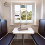 Dining area with table and bench under window. On table: tray with glasses and water bottle.