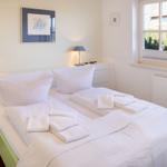 Bedroom with double bed, white linens, and window view of greenery.