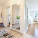 Entrance area with view into kitchen and dining room with wooden floor and window.