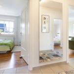 Hallway with view into bedrooms and living area. Wooden floors and rugs visible.