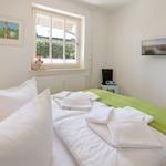 A bedroom with white bedding, green blanket edge, and view of greenery through the window.